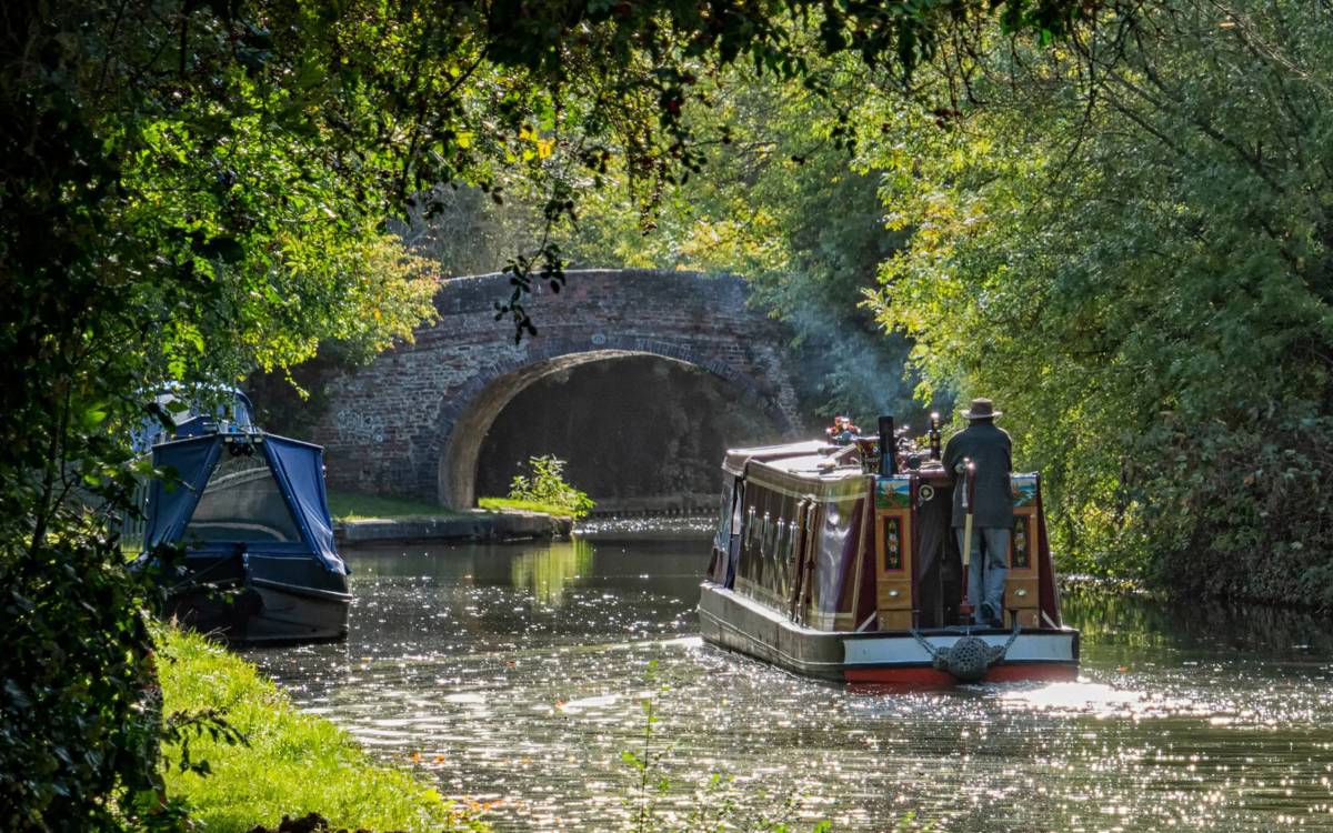 Canal boat travelling along the Grand Union Canal and heading towards a bridge