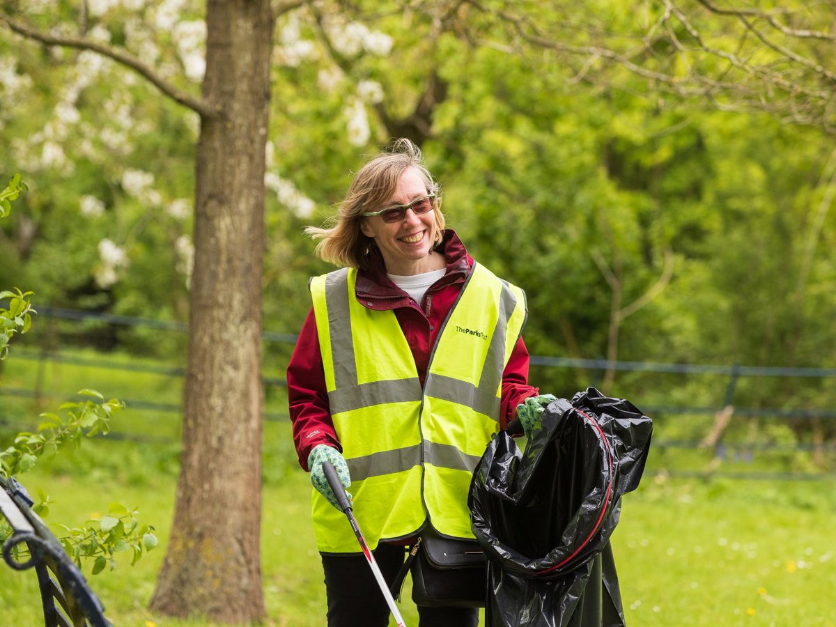 A solo female volunteer in hivis litter picking in a parkland scene